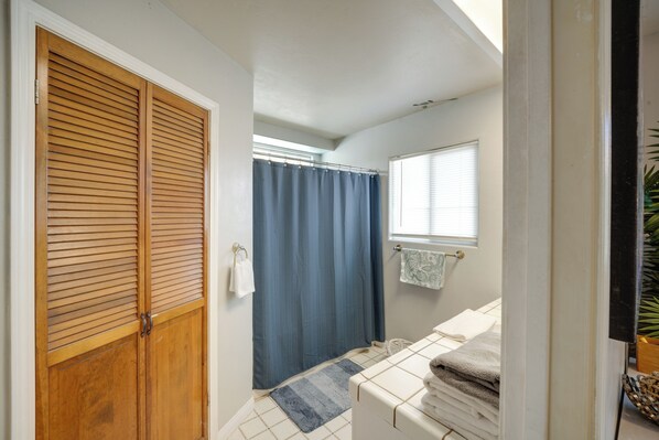 Un baño con puerta de madera, cortina de ducha azul, toallero blanco y una ventana pequeña.