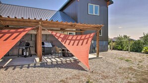 A covered patio area with a grill and outdoor seating, adjacent to a large building with a metal roof. - Pet-friendly Choteau Townhouse With Gas Grill! (Choteau)
