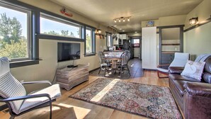 A spacious living area with a dining table, a leather couch, and a large window offering a view of the outdoors. - Pet-friendly Choteau Townhouse With Gas Grill! (Choteau)