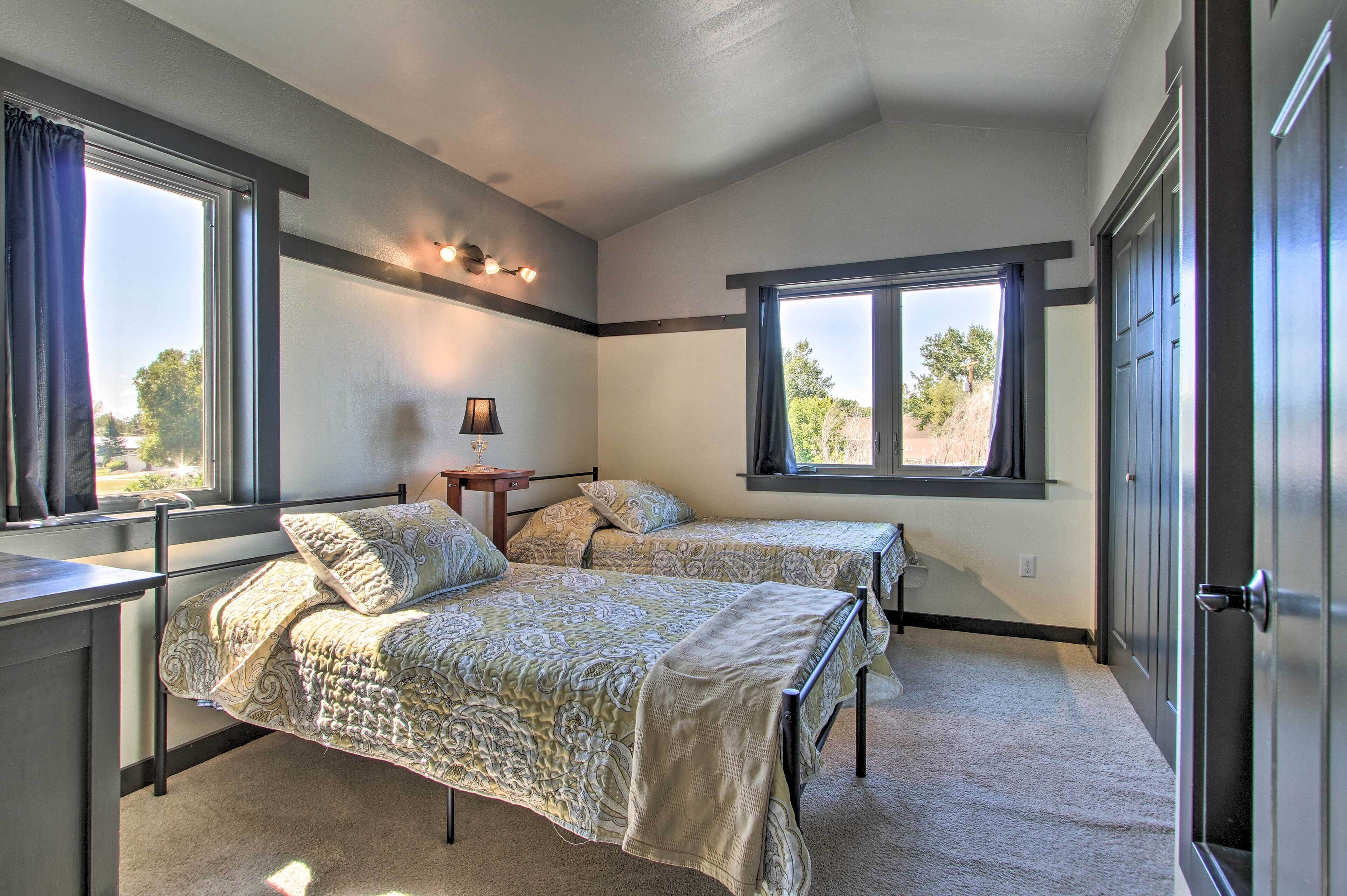 A bedroom with two beds, a desk, and a window with curtains.