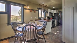 A modern kitchen with a dining area, featuring a central island, white cabinets, and a large window providing natural light. - Pet-friendly Choteau Townhouse With Gas Grill! (Choteau)