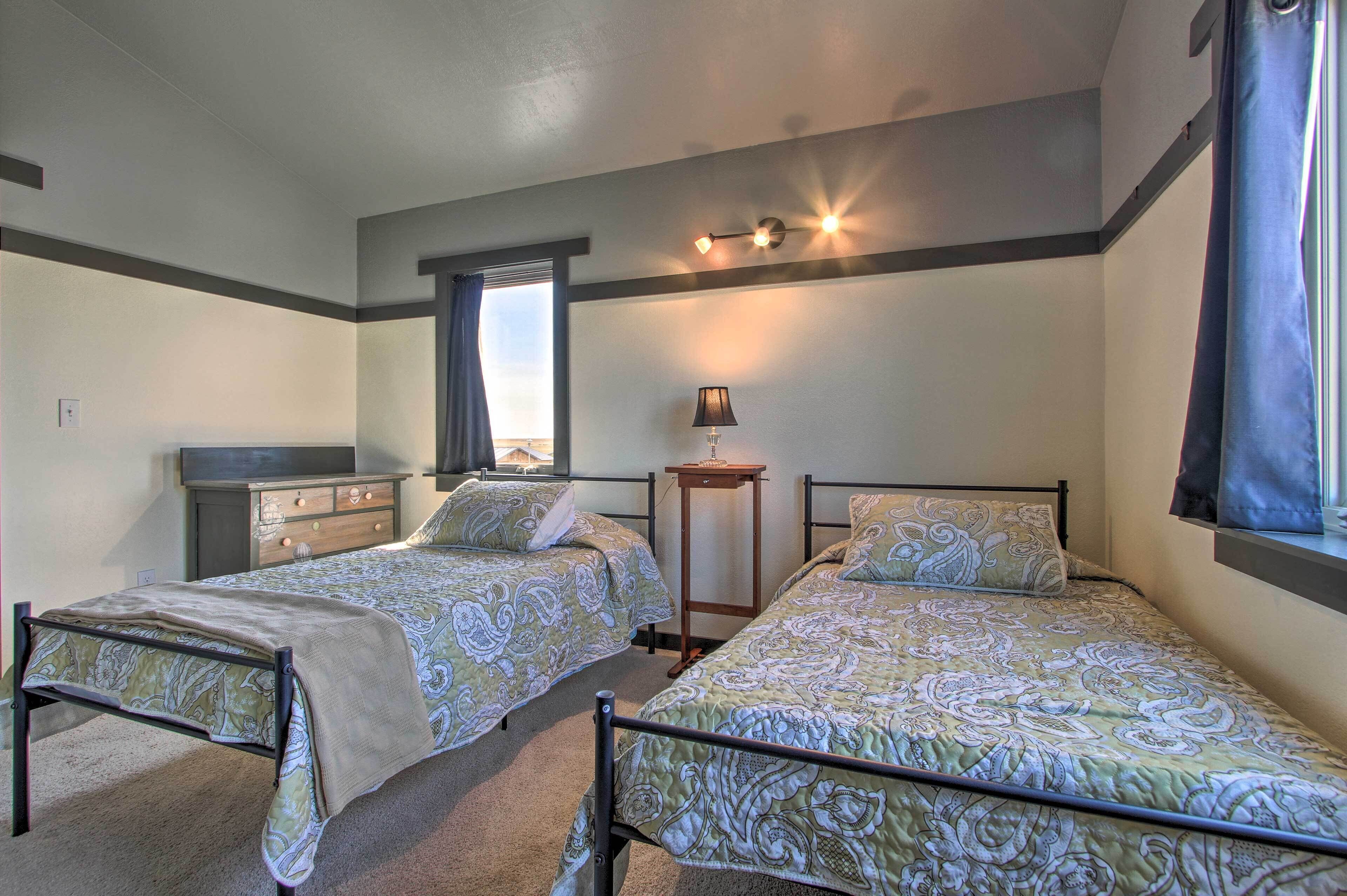 Une chambre à deux lits, avec deux lits simples, une commode, une lampe et une fenêtre.