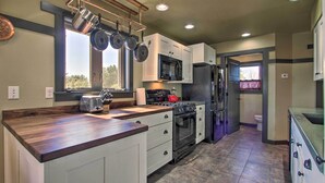 A kitchen with white cabinets, a stainless steel refrigerator, a microwave, a stove, and a hanging pot rack. - Pet-friendly Choteau Townhouse With Gas Grill! (Choteau)