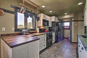 A kitchen with white cabinets, a stainless steel refrigerator, a microwave, a stove, and a hanging pot rack.
