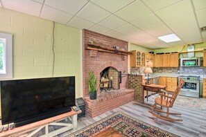 A kitchen with a brick fireplace, wooden cabinets, a microwave, and a television on a stand. - Chauga River Cabin: Renovating - Reopening mid '27 (Mountain Rest)