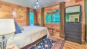 A wooden-paneled bedroom with a bed, a dresser, a mirror, and a window with curtains. - Chauga River Cabin: Pets Welcome! (Mountain Rest)
