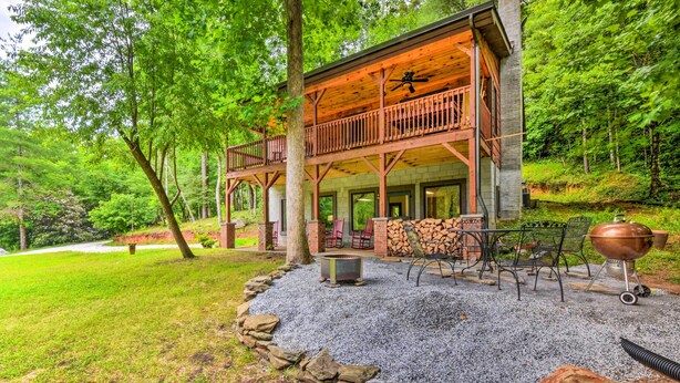A two-story log cabin with a balcony, surrounded by a gravel patio with outdoor furniture and a fire pit. - Chauga River Cabin: Pets Welcome! (Mountain Rest)