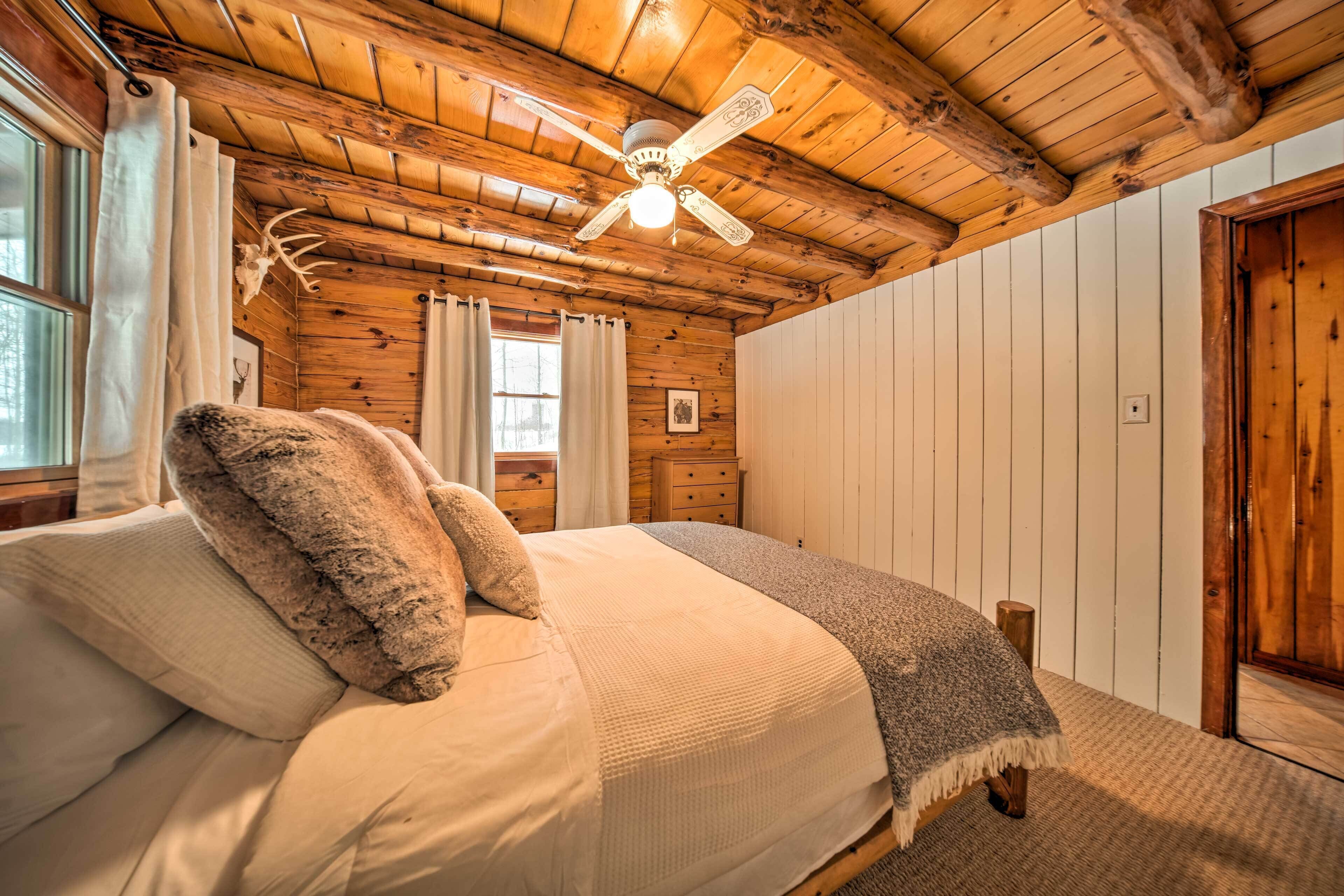 Une chambre dans une cabane en bois, avec un lit, des rideaux, un ventilateur de plafond et une porte en bois.