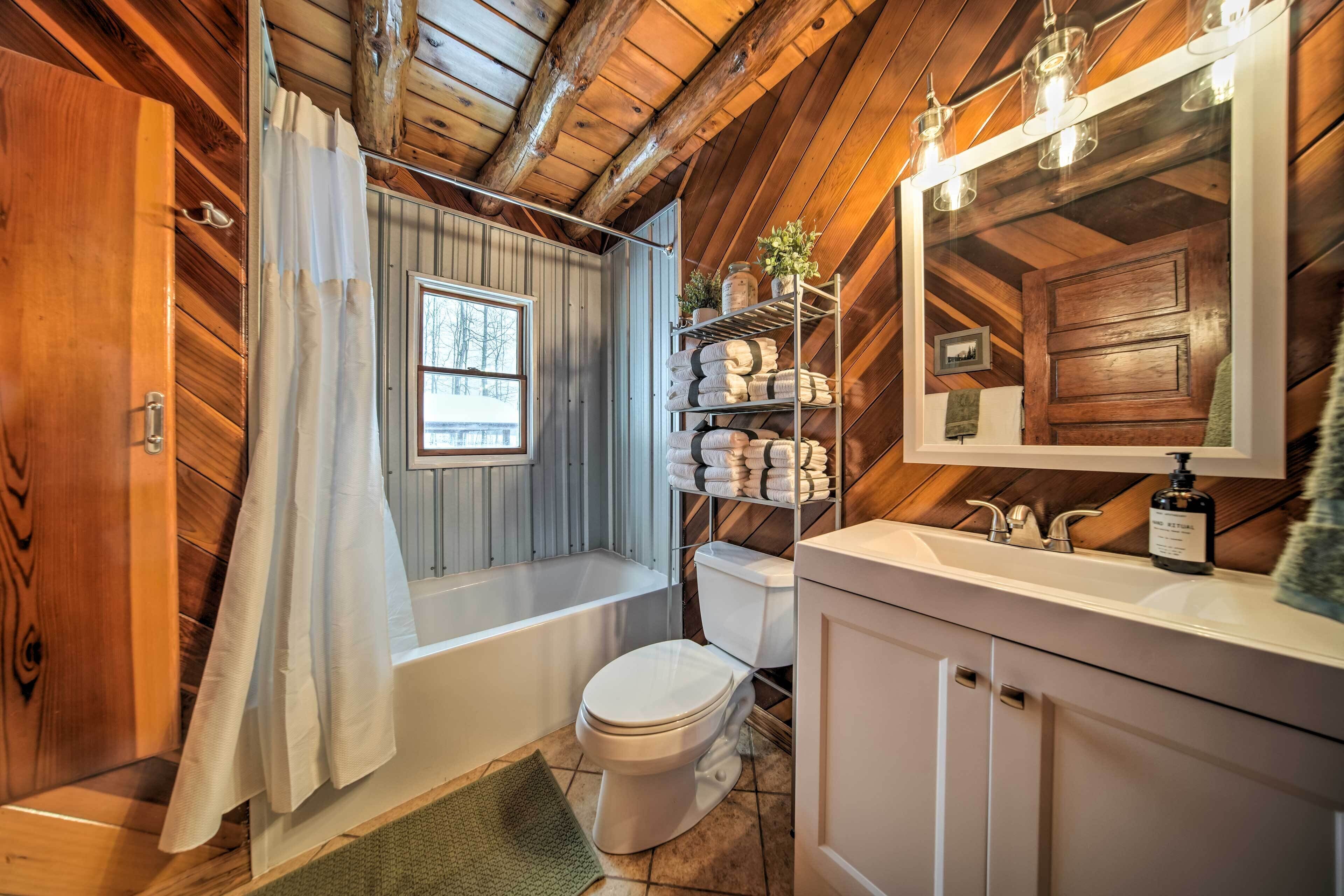 A bathroom with a wooden ceiling, a bathtub, a toilet, and a sink with a mirror.