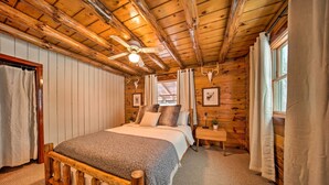 Un dormitorio de cabaña de madera con cama, mesita de noche, ventilador de techo y cráneos de ciervo colgados en la pared.