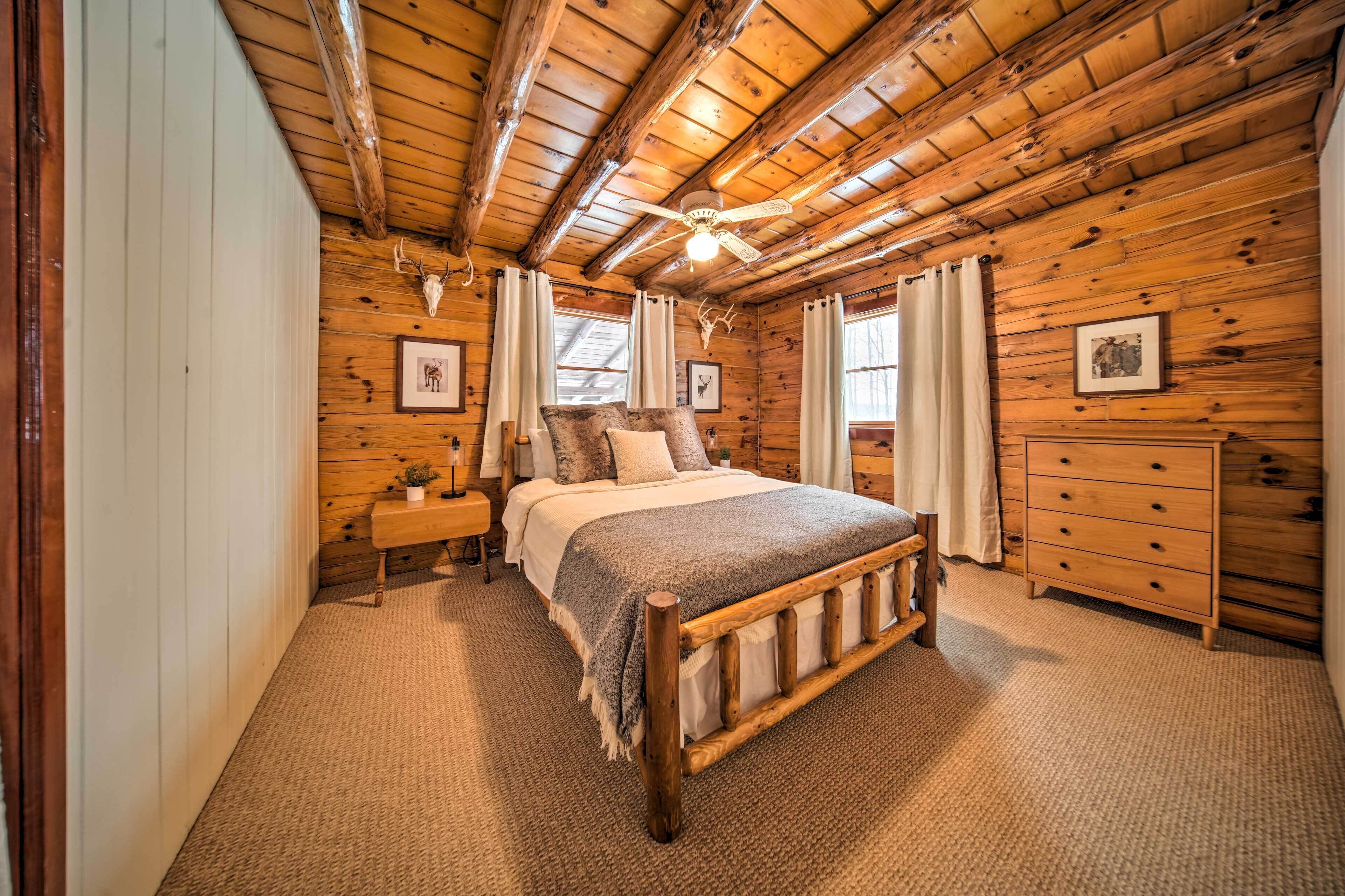 A wooden cabin bedroom with a bed, dresser, and a ceiling fan.