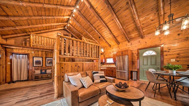 Interior acogedor de una cabaña con techo de madera, un sofá, una mesa de comedor y una escalera que lleva a un nivel superior.