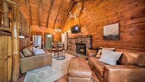 Interior acogedor de una cabaña de troncos con sofás de cuero, una chimenea de piedra y un televisor montado encima.