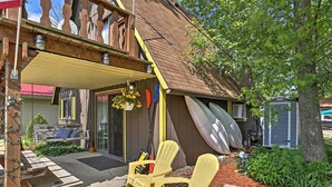 A covered outdoor seating area with Adirondack chairs, a wooden deck, and a small garden with a bench and potted plants. - Lakeview A-frame Steps to Marina & Old Field Beach (Lakeview)