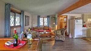A cozy living room with a sofa, patterned armchairs, a coffee table, and a dining area with a table set for two. A kitchen is visible in the background. - Lakeview A-frame Steps to Marina & Old Field Beach (Lakeview)