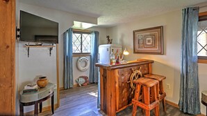 A cozy kitchen with wooden bar stools, a refrigerator, and a large window with curtains. - Lakeview A-frame Steps to Marina & Old Field Beach (Lakeview)
