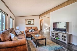 Ein Wohnzimmer mit einer Ledersofa, einem Holztisch, einem Fernseher auf einem Holzschrank und einem großen Fenster.