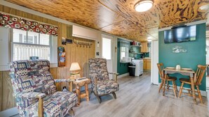 Ein gemütliches Zimmer mit Holzbalkendecke, einem an der Wand montierten Fernseher, einem Esstisch mit Stühlen und einem gemusterten Sessel.