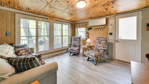 Ein gemütliches Blockhaus-Interieur mit einem großen Fenster, einer Couch, zwei gemusterten Sesseln und einer Holzbalkendecke.