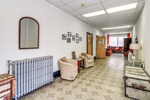 A hallway with a radiator, two chairs, a table, and a mirror.