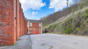 A long red brick building with a red door, a paved area in front, and a hillside with sparse vegetation. - Direct Trail Access! ATV Riding Home Base in Gary (Gary)