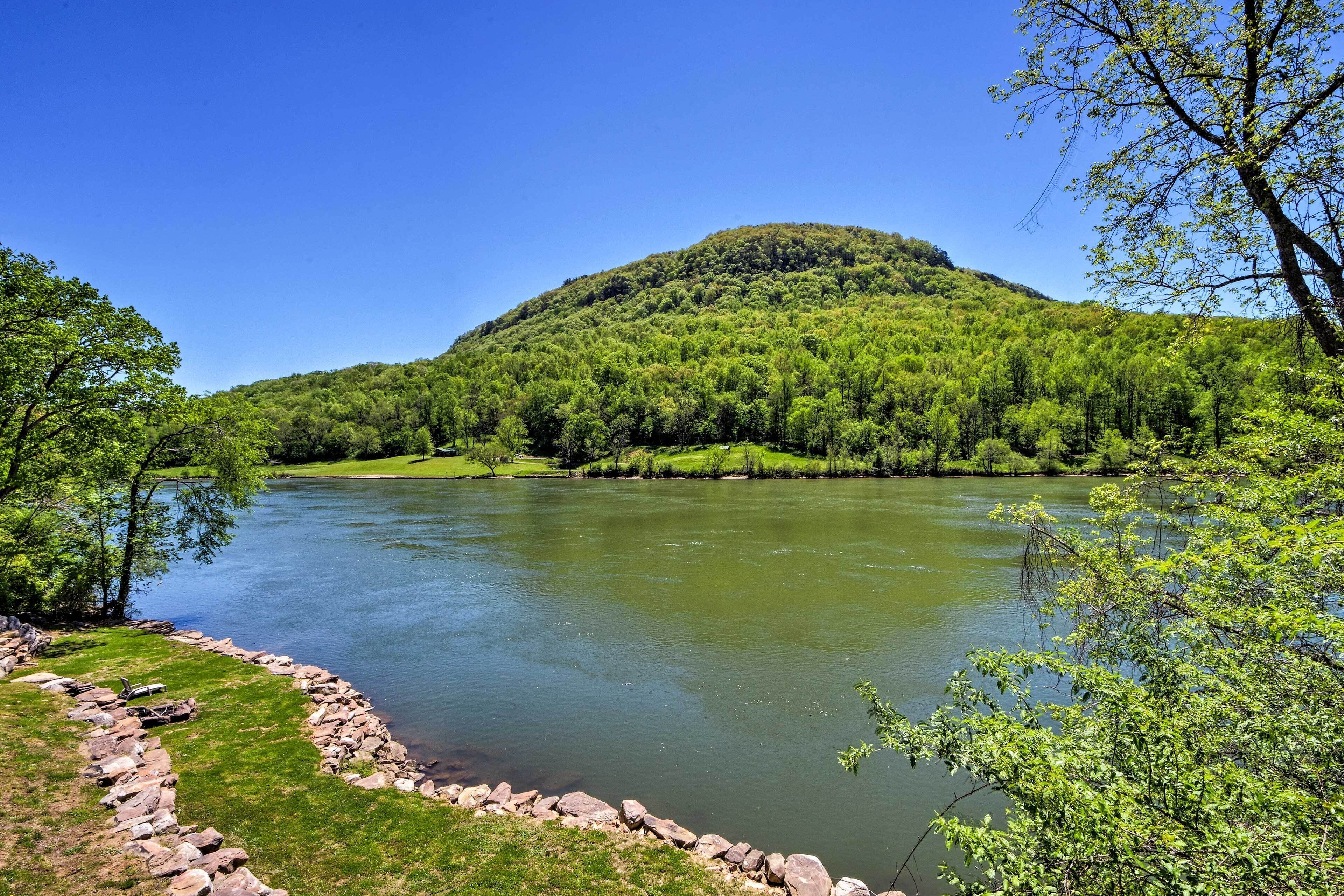 A river with a stone border, surrounded by lush greenery and a hill in the background.