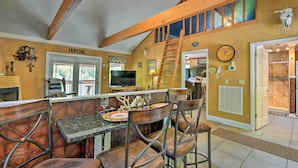 A dining area with a high wooden ceiling, a central table with chairs, and a television in the background.