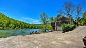 A house with a concrete driveway, a river view, and a forested hillside.
