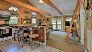 A spacious kitchen with a dining area, wooden beams, a fireplace, and a large window.