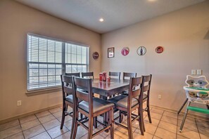 A dining area with a table set for four, surrounded by chairs, a window with blinds, and wall decorations including Coca-Cola memorabilia.