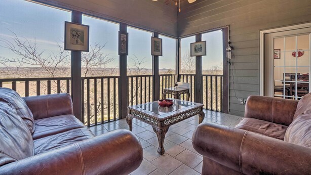 A covered patio with leather sofas, a glass-top table, and framed pictures on the walls.