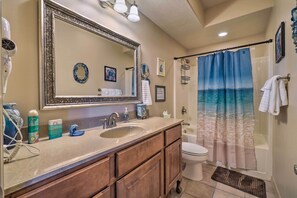 A bathroom with a large mirror, a sink, a toilet, and a shower curtain with a beach scene.