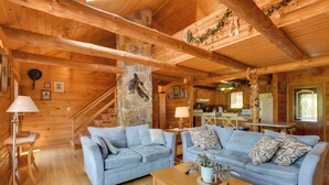 Accogliente interno di una baita in legno con due divani azzurri, un tavolino in legno e un pilastro in pietra con una statua a parete.