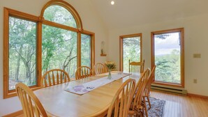 Una sala da pranzo con tavolo in legno, sedie e ampie finestre che si affacciano su una foresta.