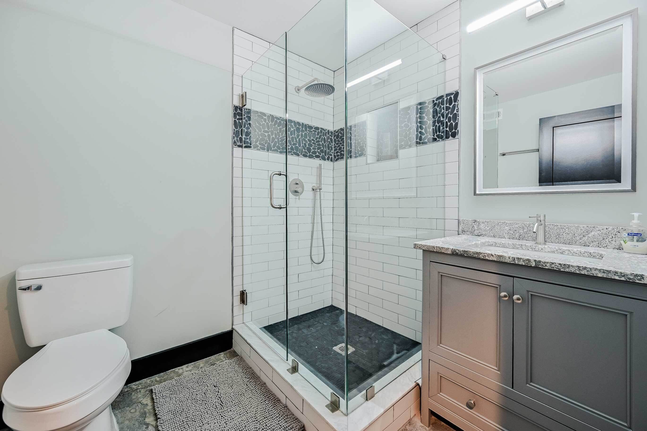 Un bagno moderno con doccia vetrata, un water bianco e un mobile lavabo in granito.