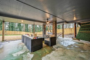 An outdoor patio with a stone fireplace, wicker furniture, and a view of a wooded area.