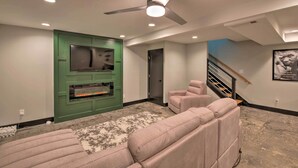 A modern living room with a green entertainment unit, a fireplace, a beige sofa, and a ceiling fan. - 5 Mi to Mercedes-benz Stadium: Stylish ATL Retreat (Atlanta)