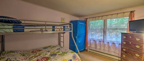 A room with bunk beds, a dresser, and a window with curtains.