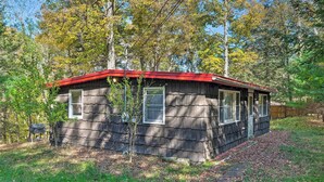 A small cabin with a red roof, surrounded by trees and a grassy yard.