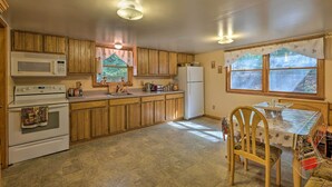 A compact kitchen with wooden cabinets, a microwave, a stove, a refrigerator, and a dining table with chairs.