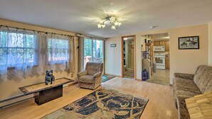 A spacious living room with a large window, a fireplace, and a kitchen in the background.