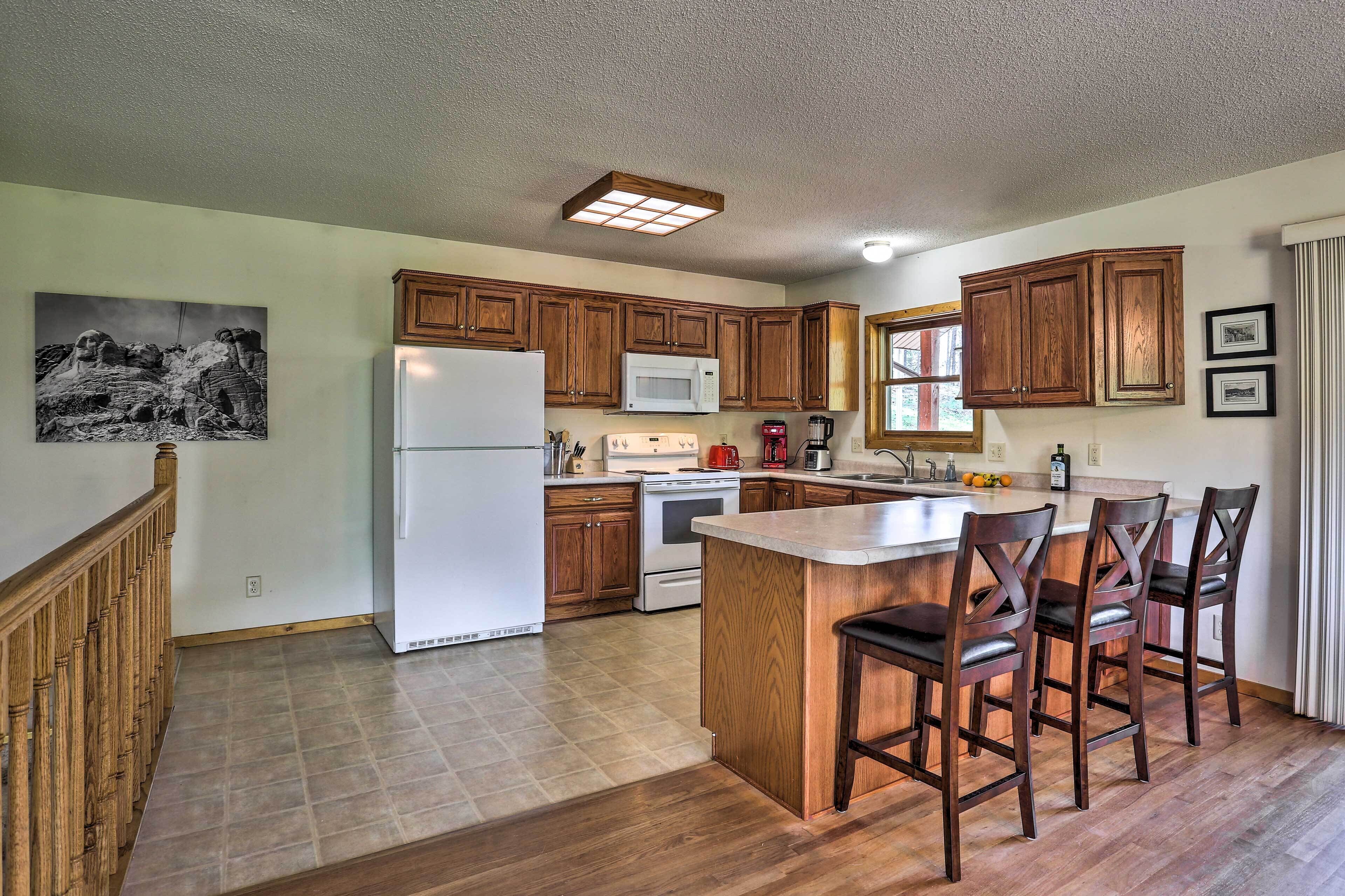 A kitchen with wooden cabinets, a white refrigerator, a microwave, a stove, and a bar area with stools.