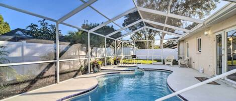 A covered swimming pool with a glass roof, surrounded by a concrete deck and a white fence.