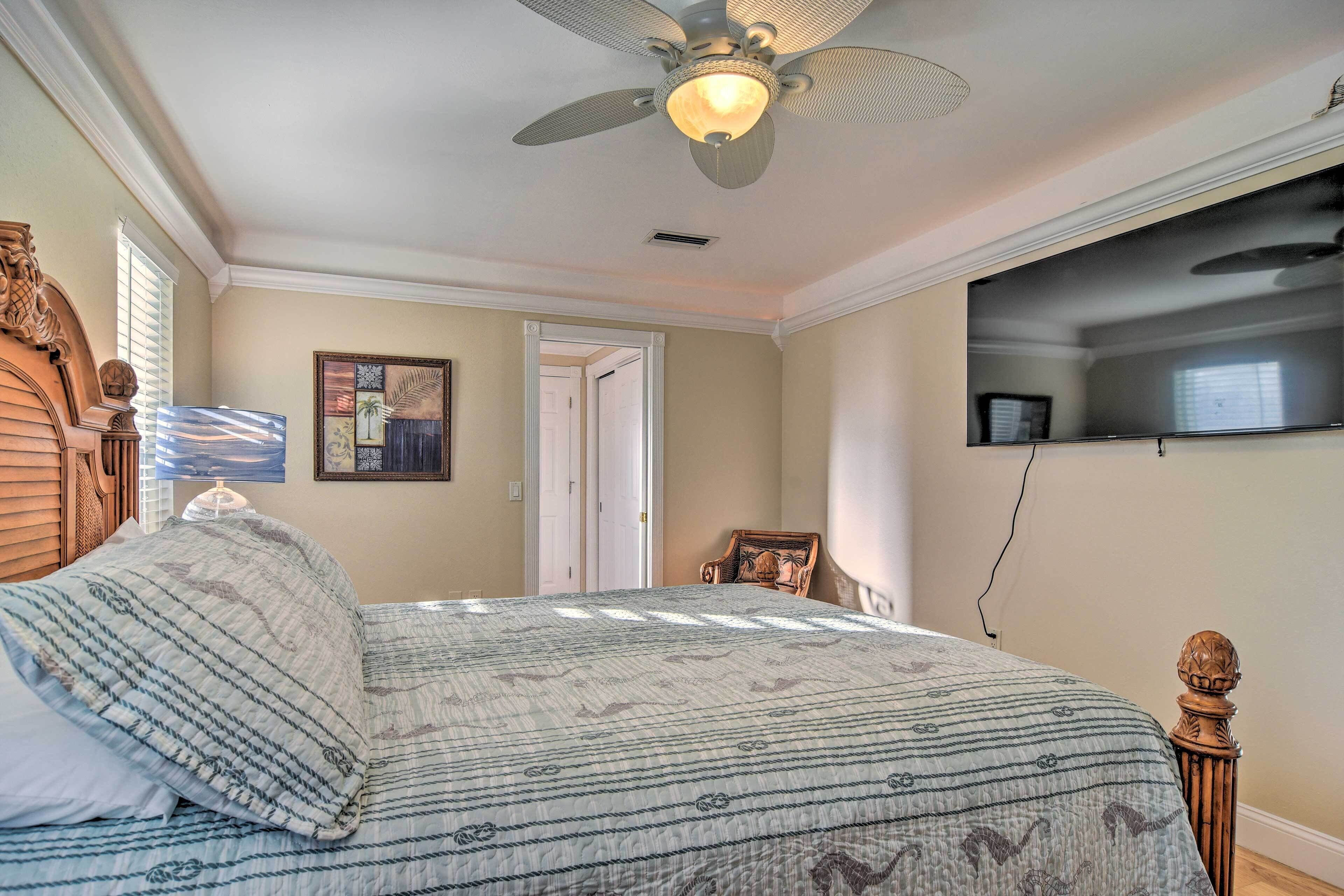 A bedroom with a bed, a ceiling fan, a television mounted on the wall, and a door leading to another room.