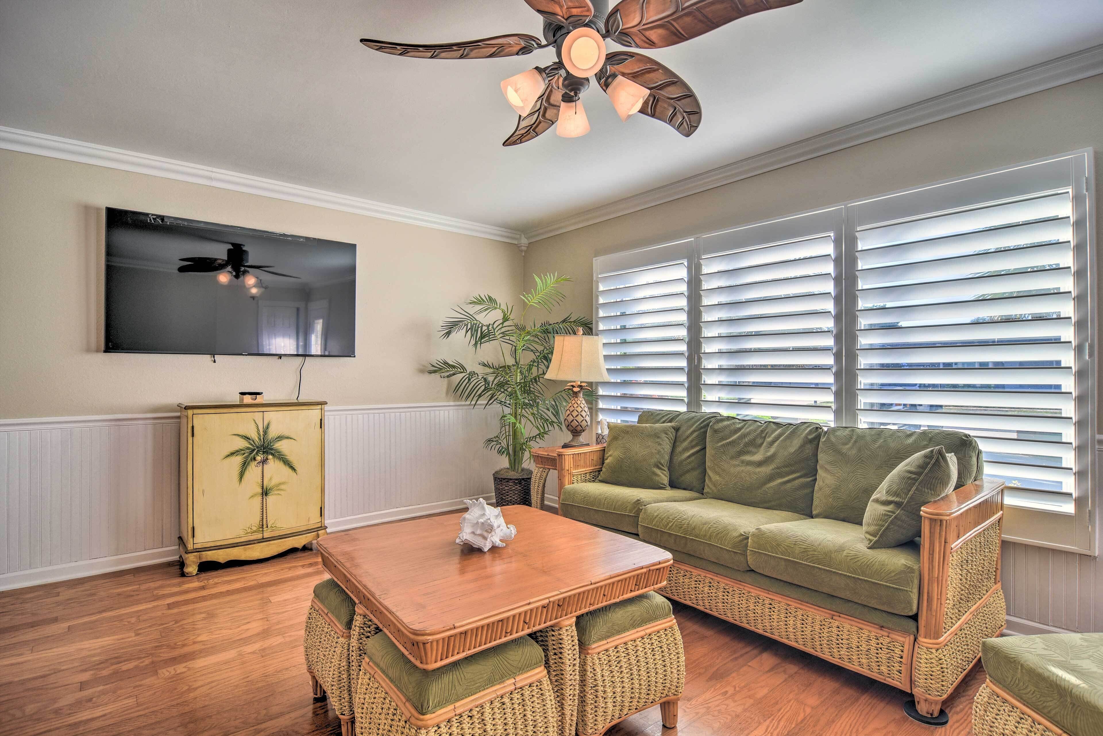 A living room with a wooden coffee table, green sofa, wicker chairs, a television, and a ceiling fan.