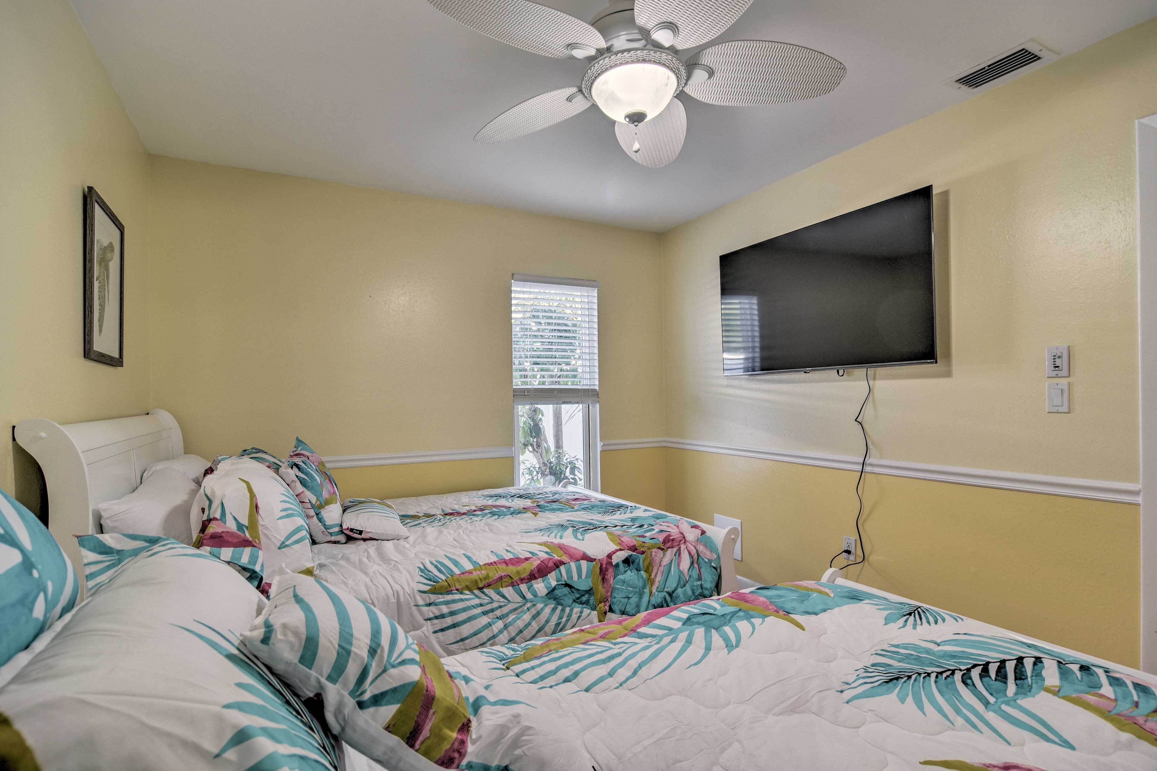A bedroom with two beds, a ceiling fan, a TV mounted on the wall, and a window with blinds.