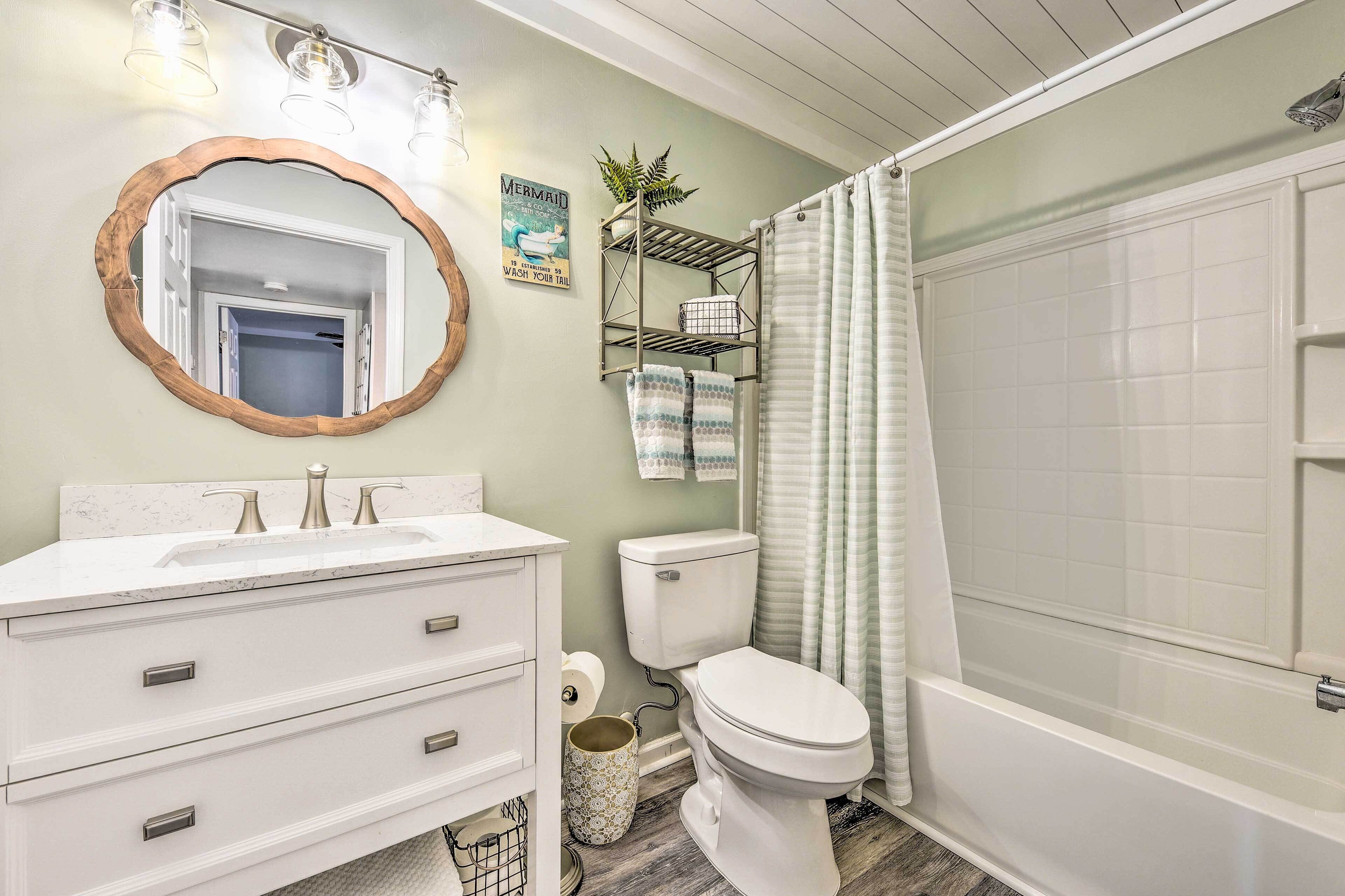 A bathroom with a white vanity, a round mirror with a wooden frame, a toilet, and a bathtub.