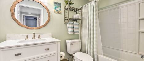 A bathroom with a white vanity, a round mirror with a wooden frame, a toilet, and a bathtub.
