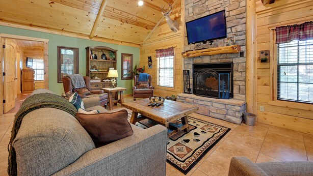 Un acogedor interior de cabaña de madera con chimenea de piedra, muebles de madera y un televisor montado encima.