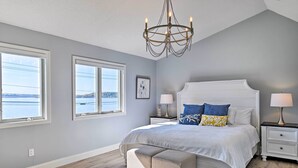 A bedroom with a large bed, two bedside tables, a chandelier, and a view of the water. - Charming Saratoga Lake Retreat w/ Dock Access (Saratoga Springs)